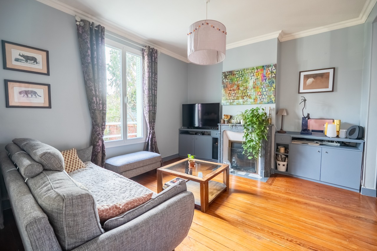 JLHECBD4UOMPPiBe0mEjaWmVghOOtcRsL6D2rVoY.jpg Salon avec murs gris, canapé gris, cheminée, parquet massif